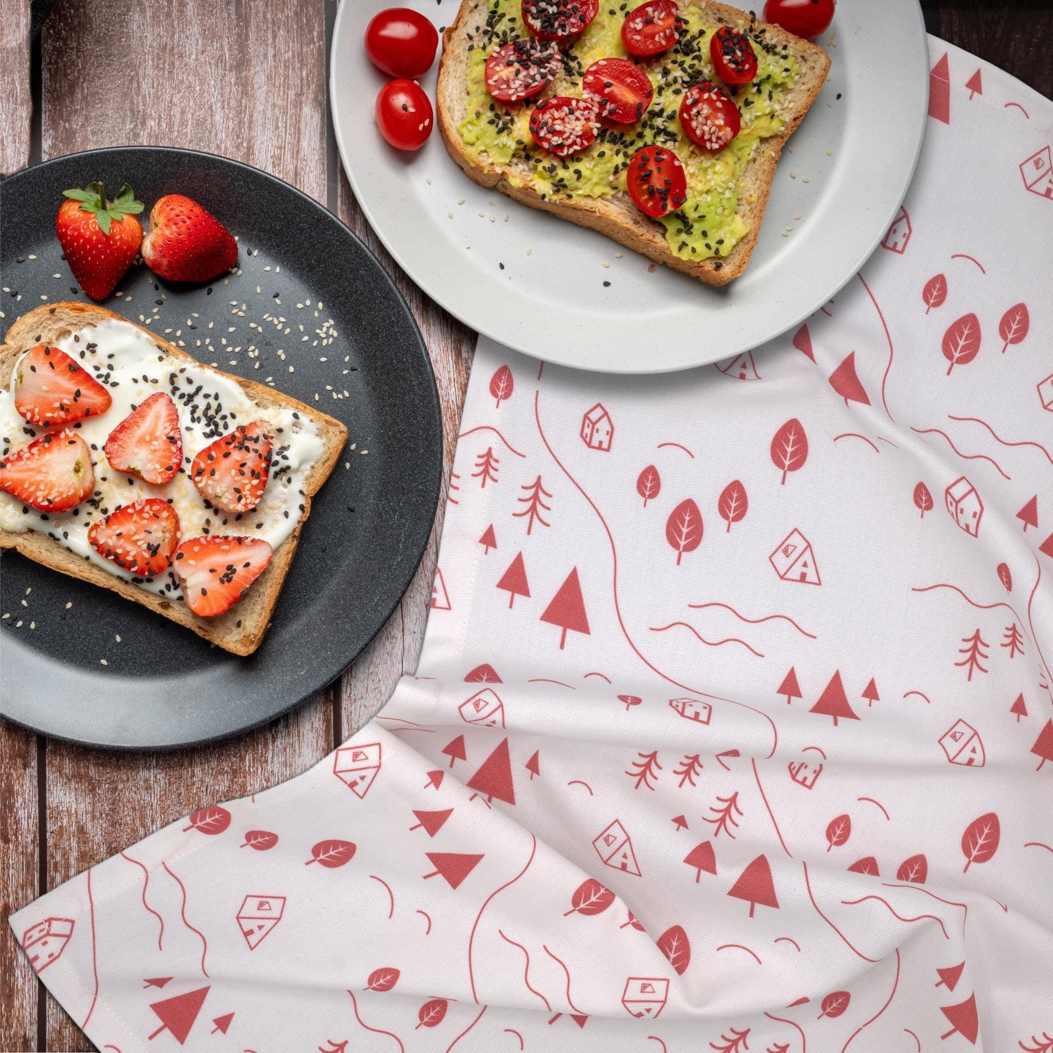 Two plates of toast with strawberries and avocado on a wooden surface with a patterned tiny countryside kitchen towel from Hem And Tassel 