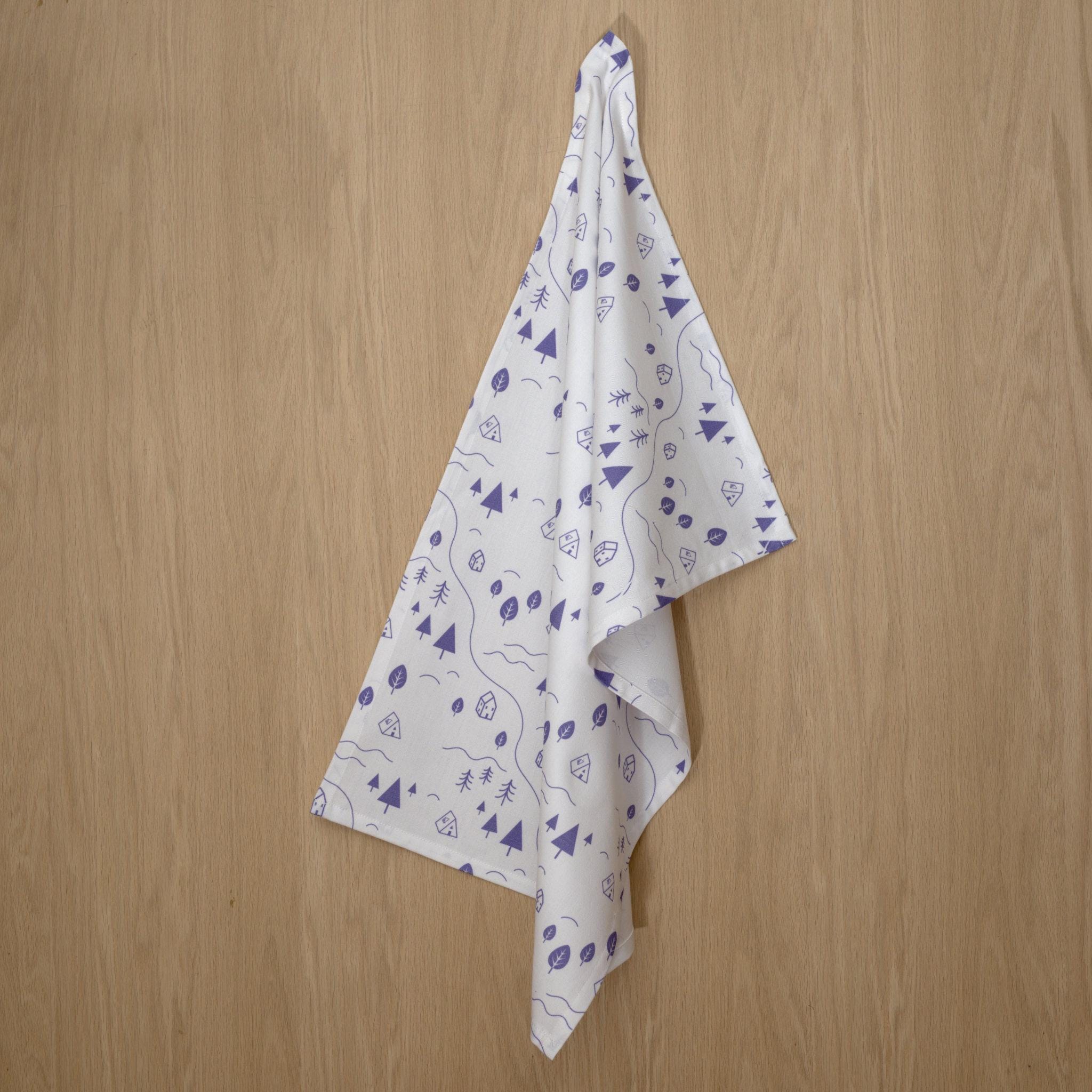 White tiny countryside kitchen towel with purple patterns hanging on a wooden wall from Hem And Tassel 