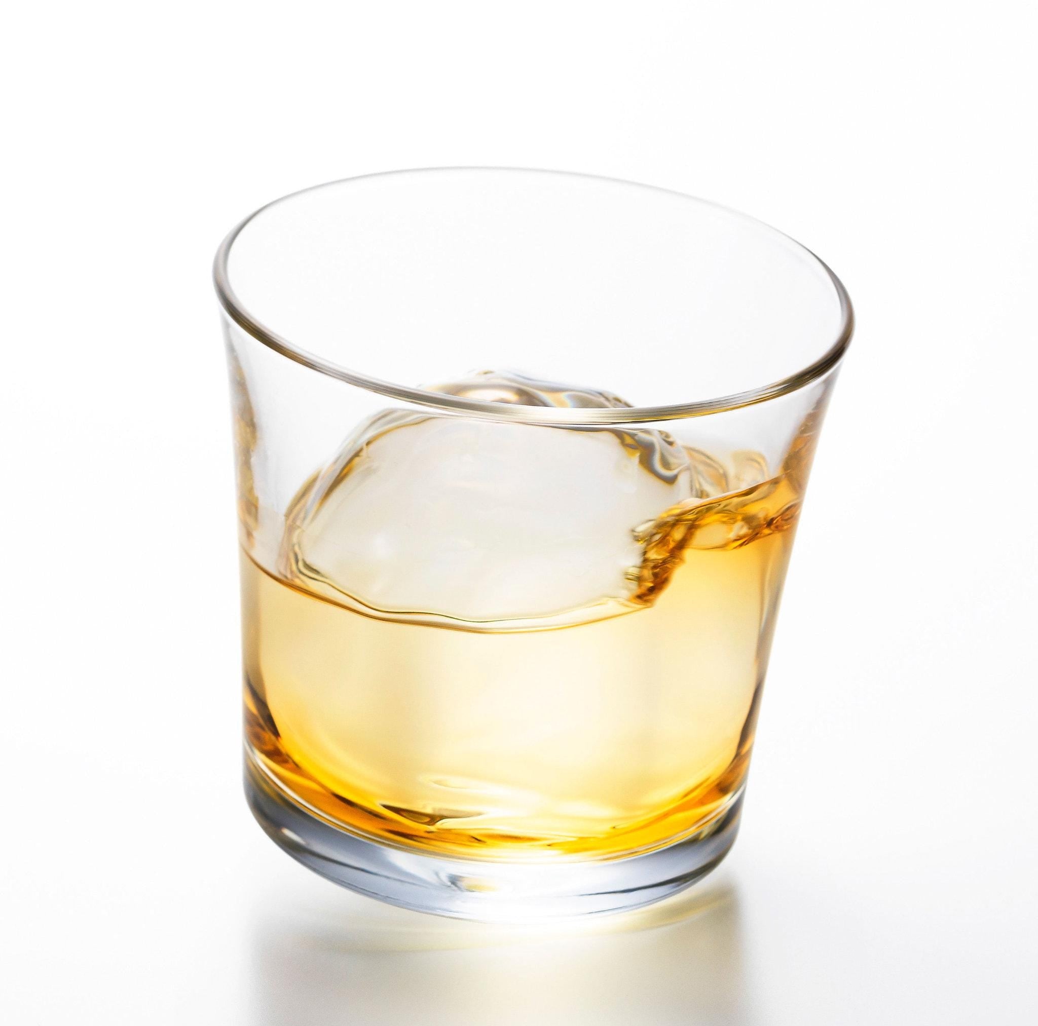 made in Japan designer tottering whiskey glass with whiskey and ice in it from Hem And Tassel, sitting inclined on a white background