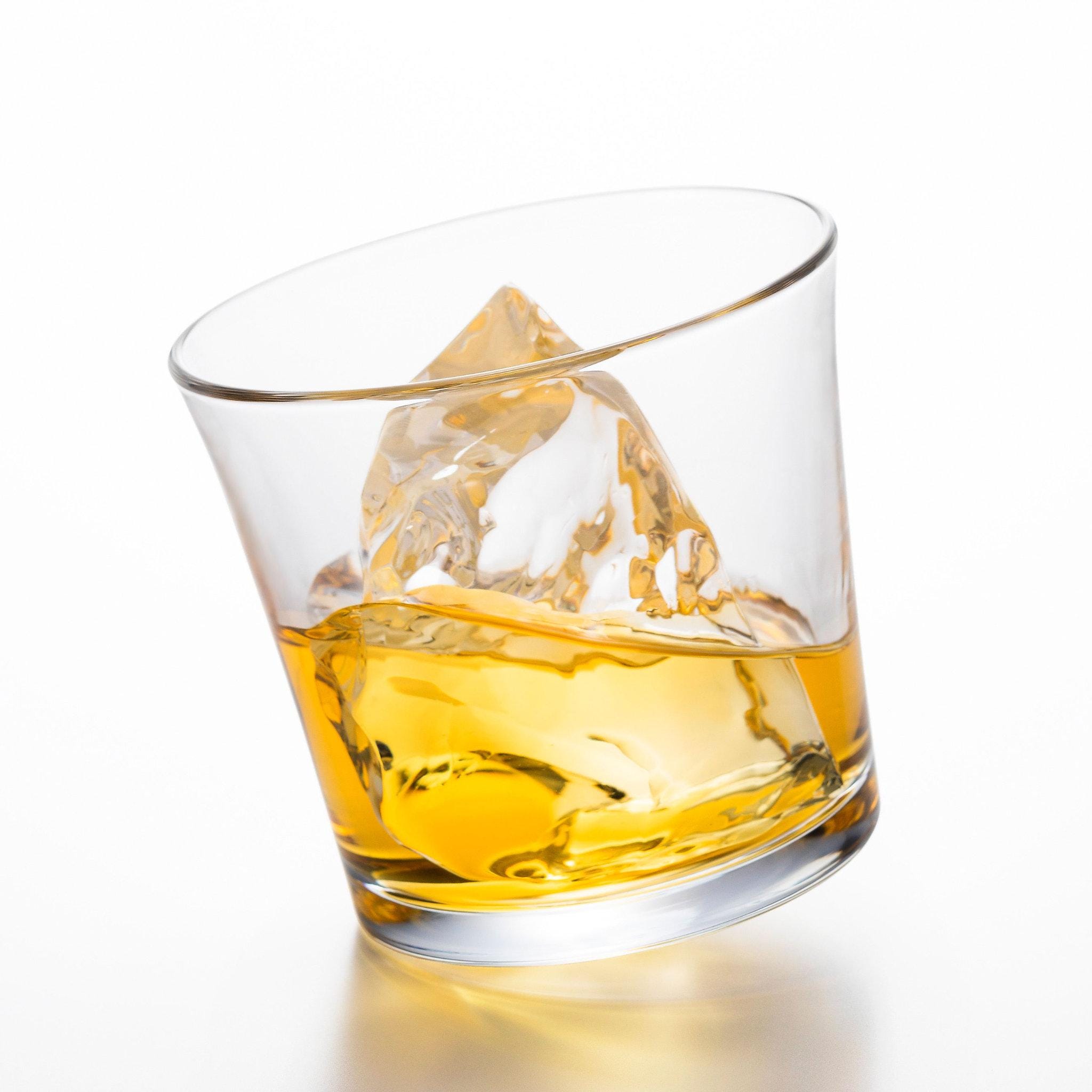 made in Japan designer tottering whiskey glass with whiskey and ice in it from Hem And Tassel, sitting inclined on a white background