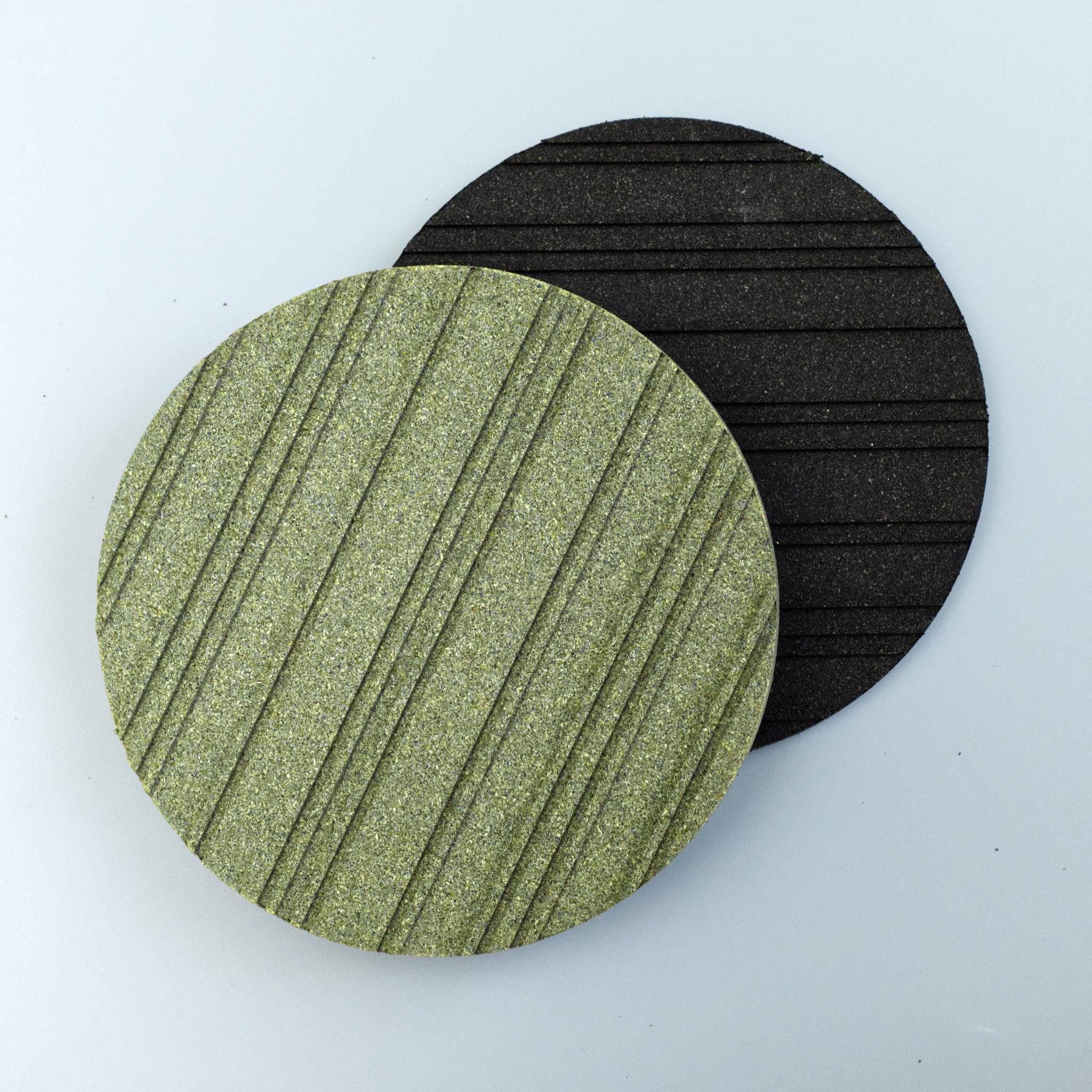 Two circular heatsink cork trivets, one green and one black, on a light blue background from Hem And Tassel 