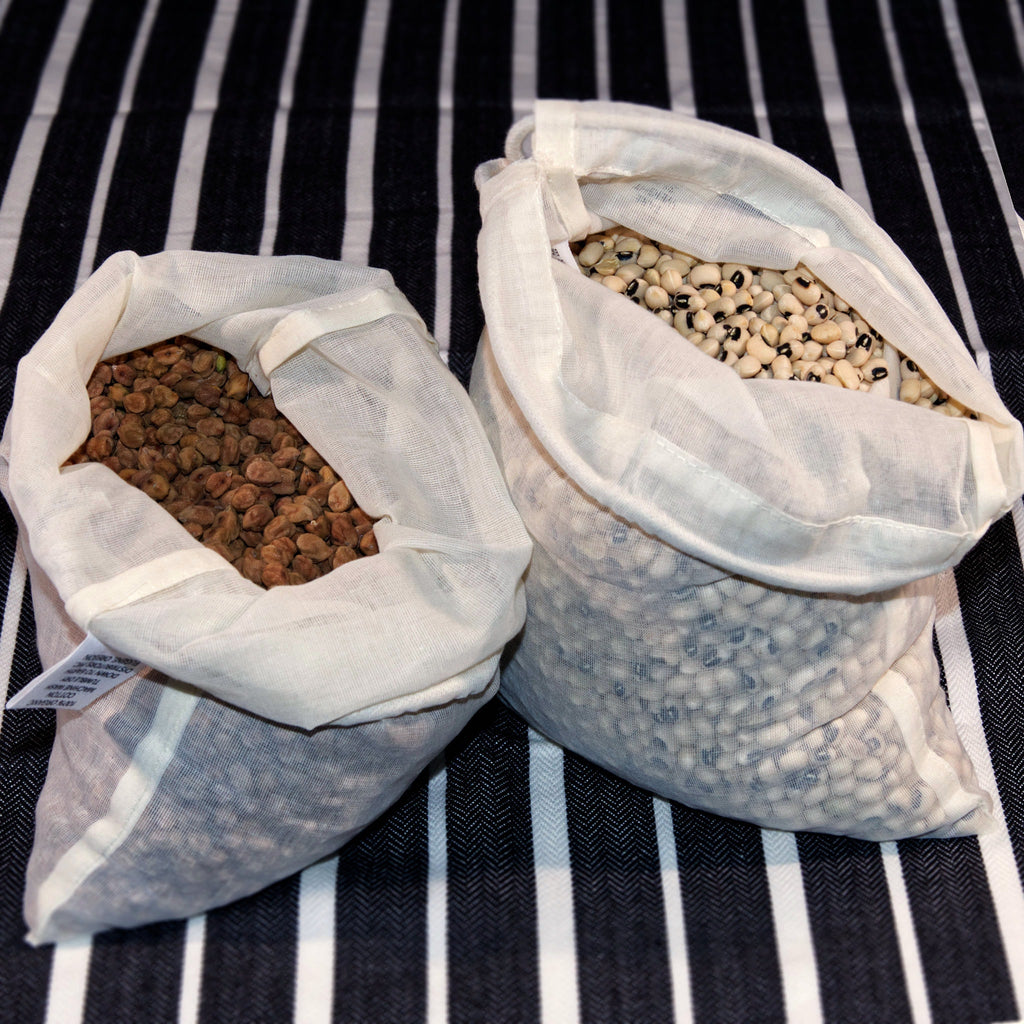 Two open organic cotton produce bags filled with seeds on a back and white striped background from Hem And Tassel 