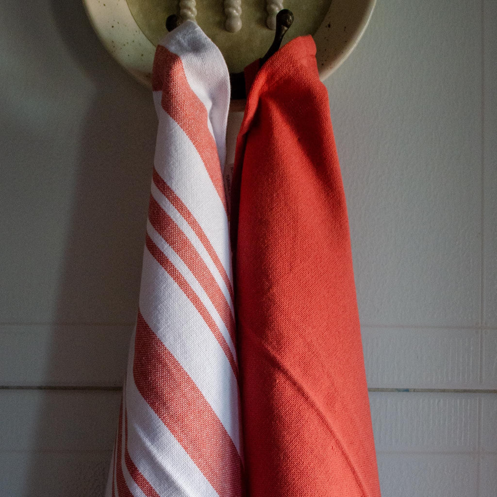 Red solid and white striped towel hanging on a hook against a tiled wall from Hem And Tassel 