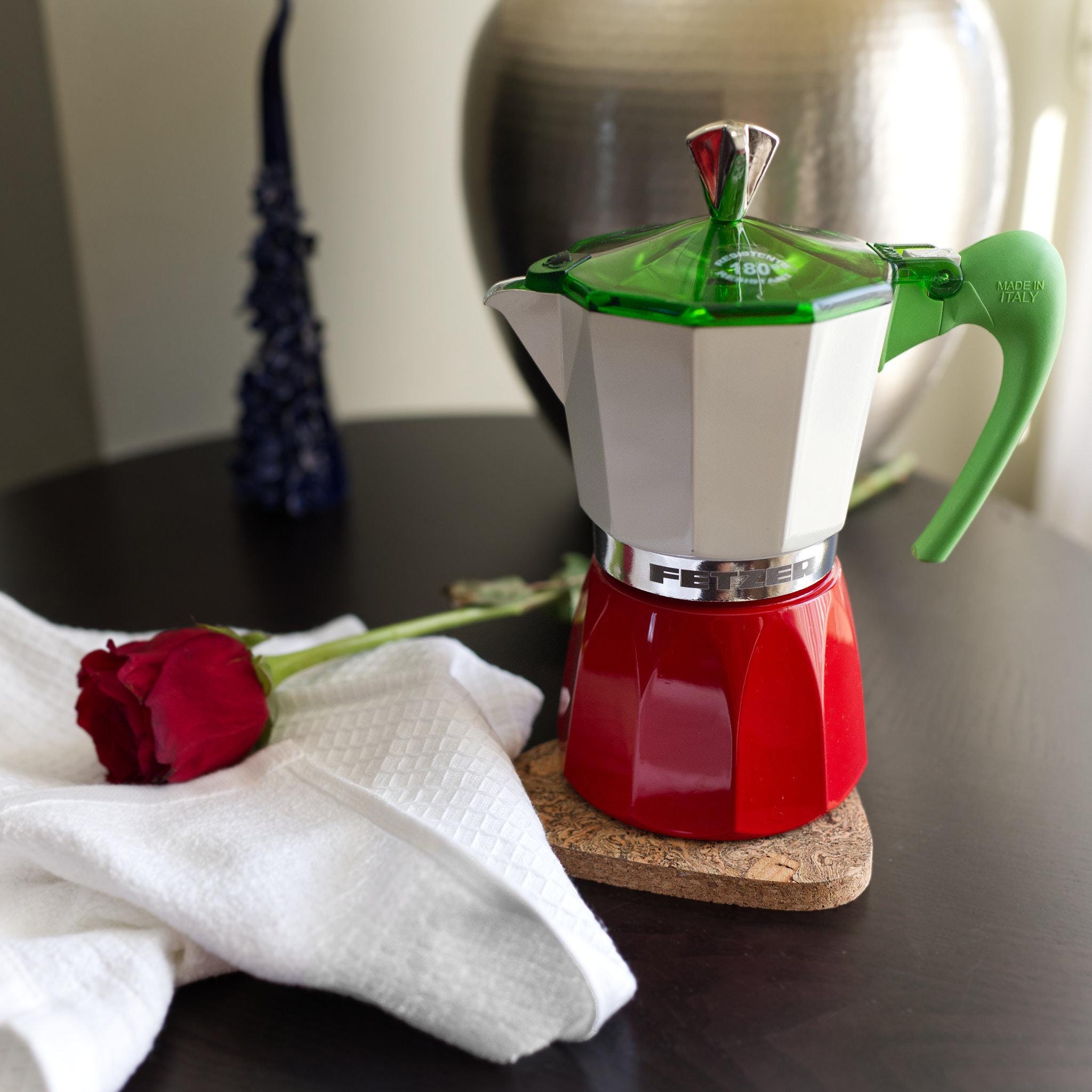 Red and green coffee maker on a table with a red rose and white  Jekyll and Hyde kitchen towel showing the waffle and Terry surfaces both