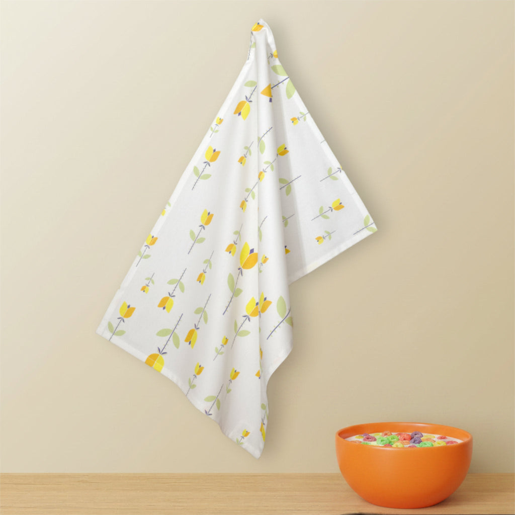 A white kitchen towel with a yellow tulip pattern hangs on a beige wall above a wooden surface, with an orange bowl of colorful candies in the lower right corner from Hem And Tassel