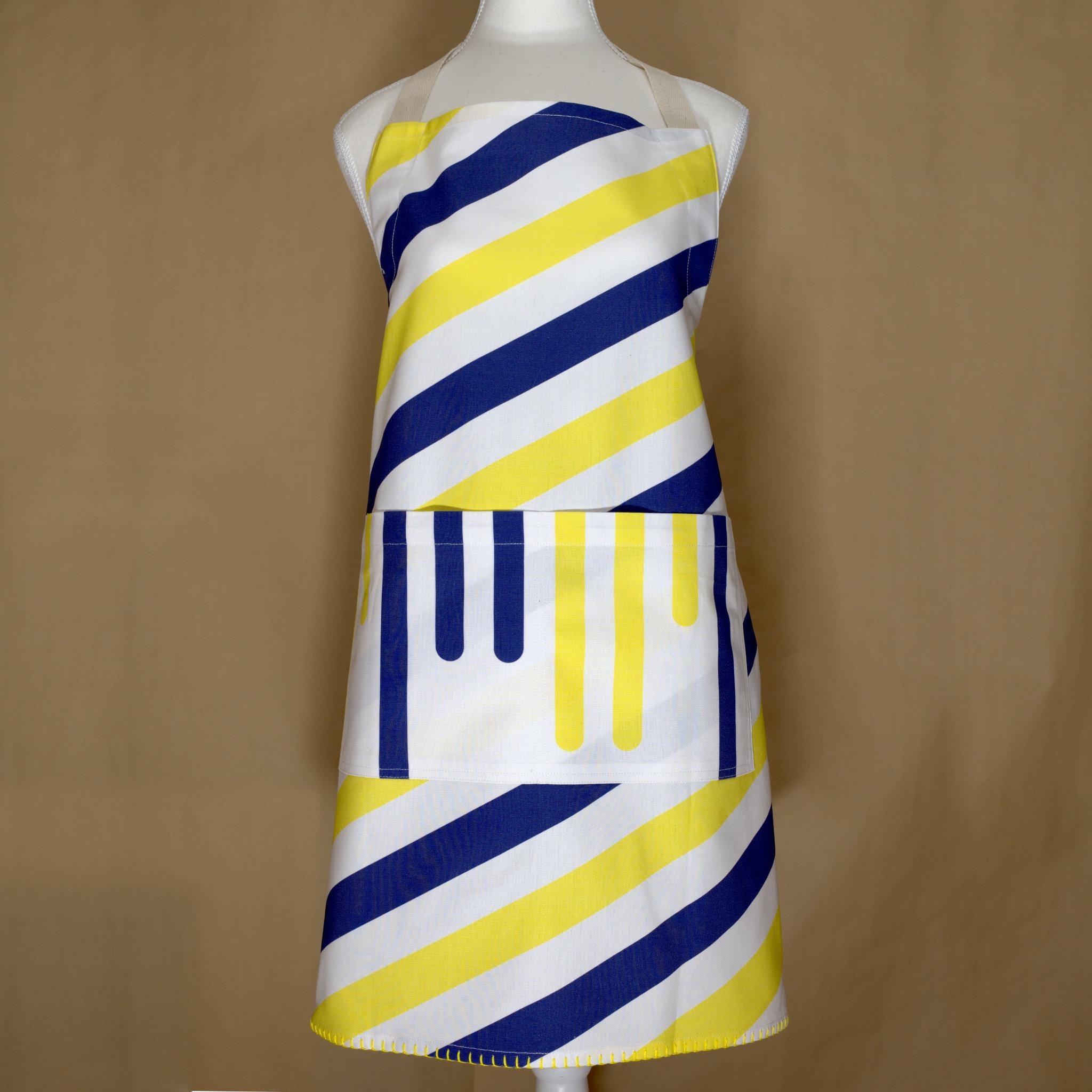Yellow piano striped apron with blue and yellow pattern on a mannequin against a brown background from Hem And Tassel 