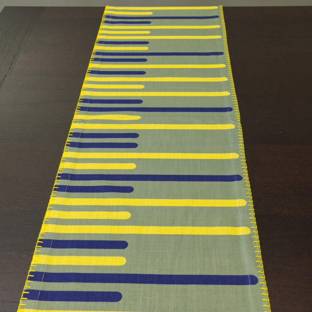 yellow piano table runner with blue and yellow striped pattern on a dark surface from Hem And Tassel 