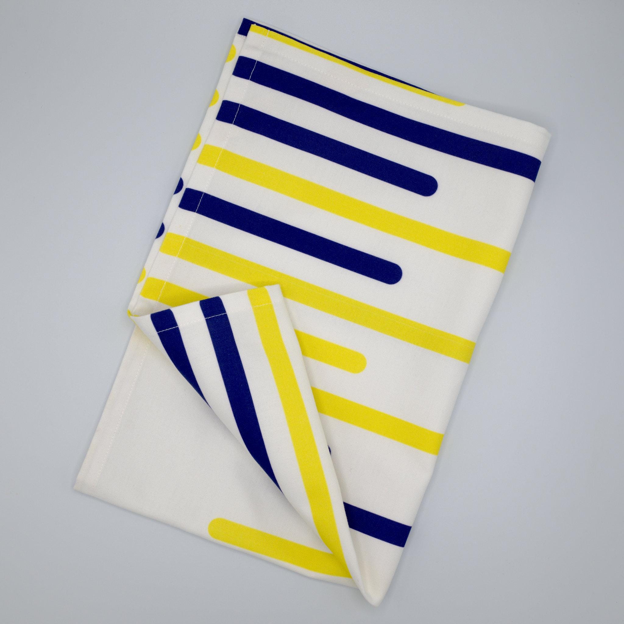Folded yellow piano tea towel with horizontal  blue and yellow stripes on a gray background from Hem And Tassel 