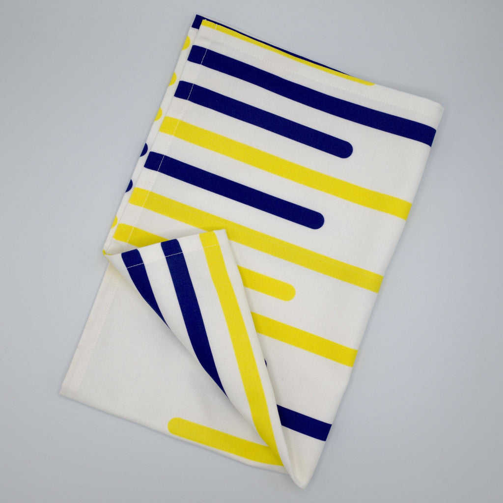 Folded yellow piano tea towel with horizontal  blue and yellow stripes on a gray background from Hem And Tassel 