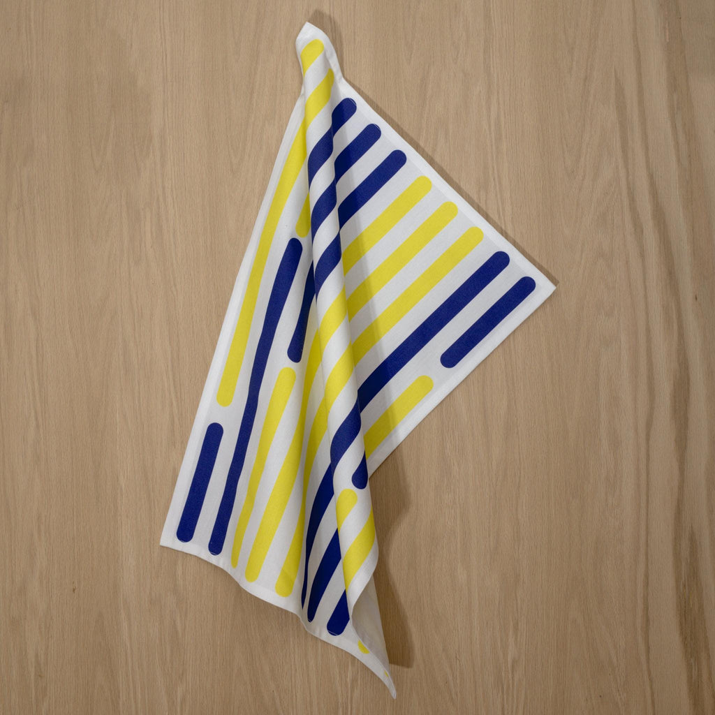 Striped yellow piano tea towel with vertical blue and yellow lines on a wooden surface from Hem And Tassel 