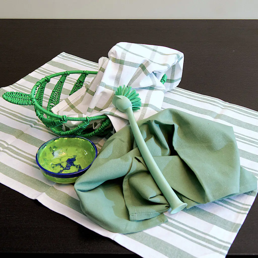Three large 100% cotton kitchen towels in flat weave shown on a dining table , of decade classics style, in solid green, checks and stripes