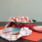 Three large 100% cotton kitchen towels in flat weave shown on a table, of decade classics style, in red blue, checks and stripes