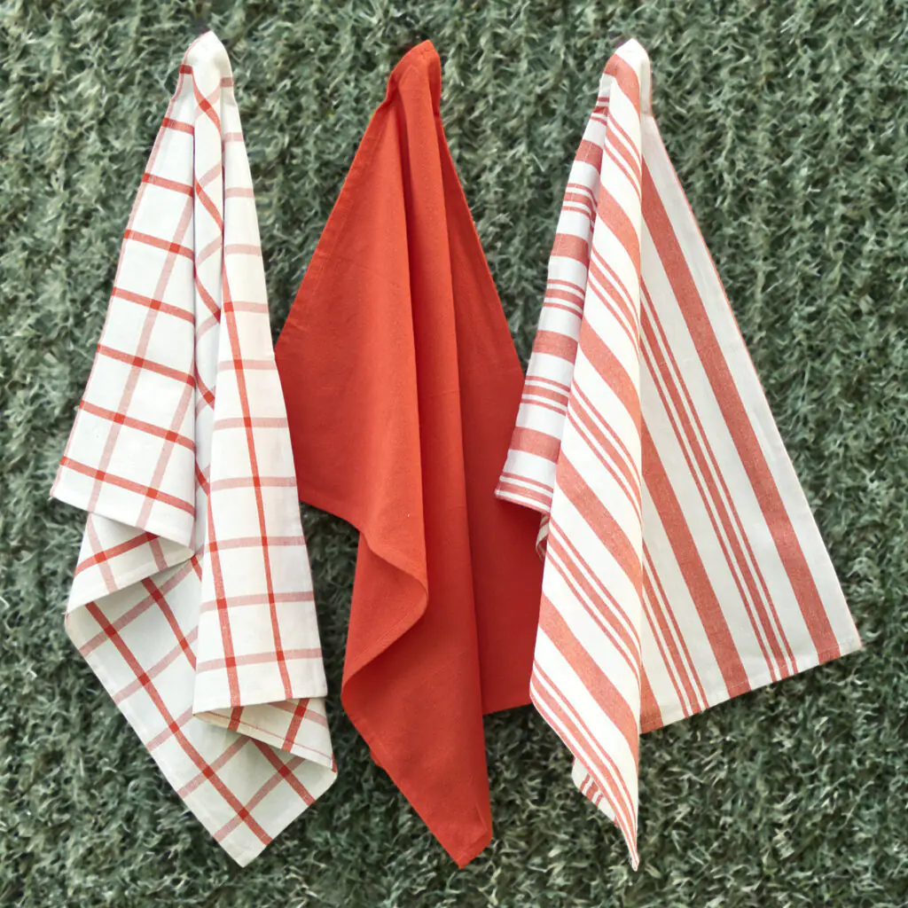 Three large 100% cotton kitchen towels in flat weave shown hanging, of decade classics style, in solid red, checks and stripes