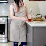 Girl wearing, pro-grade, heavy duty, drill cotton cooking and baking Apron, in grey with divided pocket and with adjustable neck straps. With matching oven mitt and pot holder