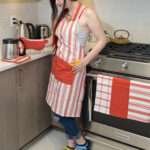 Girl wearing apron with full bundled set visible. Everyday cooking and baking Apron in Classic red stripes and solid red divided pocket with Adjustable neck straps, set of 3 towels, oven mitt and pot holder