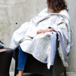 Throw From Europe 100% Cotton Reversible Jacquard Garden pattern in blue color worn by lady on outdoor garden chair
