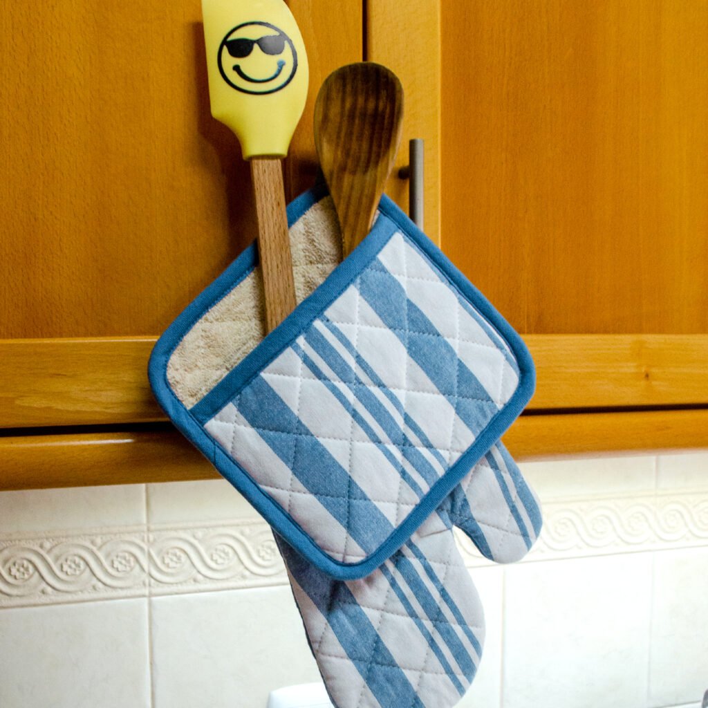 Quilted Decade classic oven mitt and pot holder shown in blue color, hanging with with striped side visible