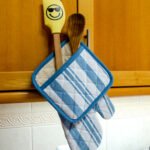Quilted Decade classic oven mitt and pot holder shown in blue color, hanging with with striped side visible
