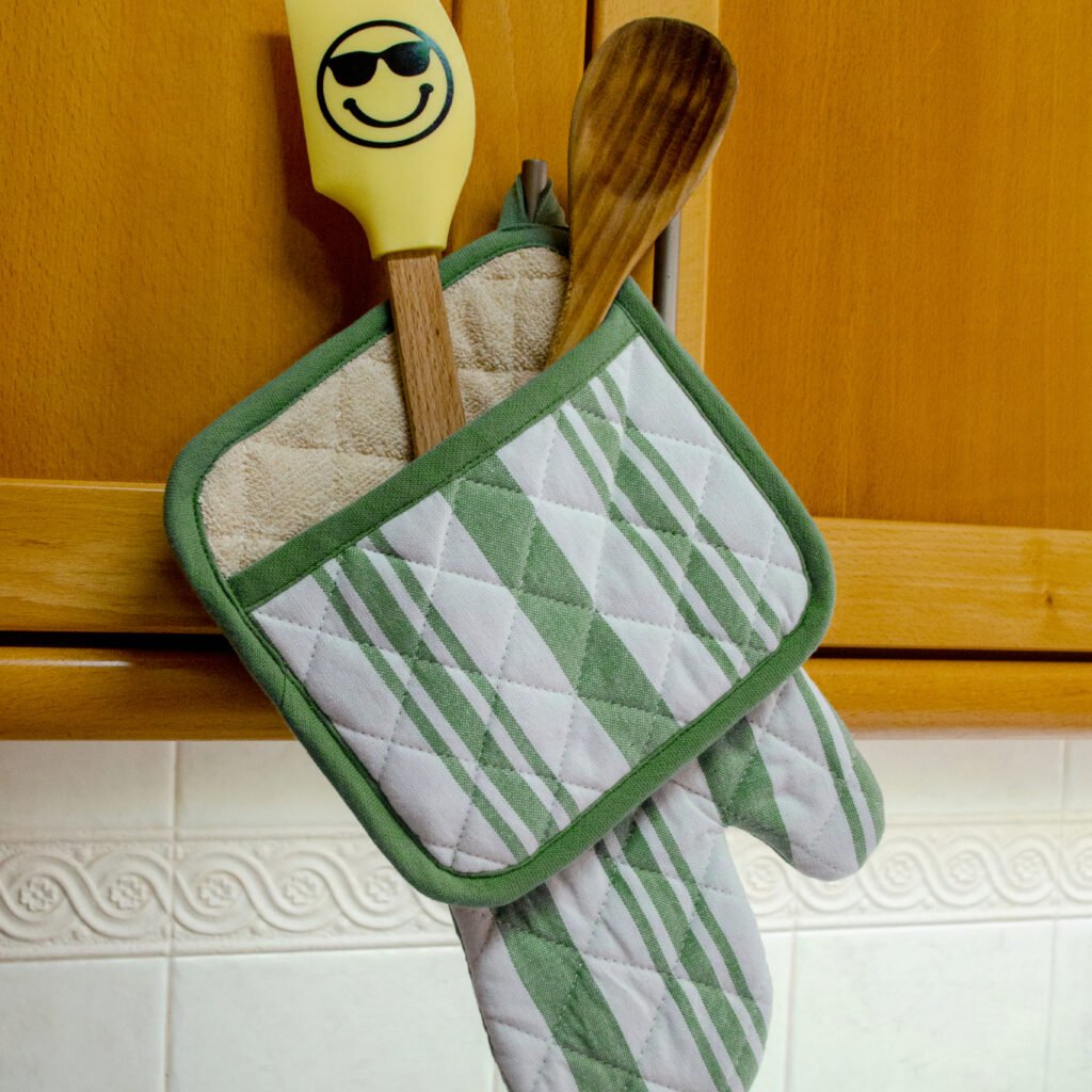 Quilted Decade classic oven mitt and pot holder shown in blue color, hanging with with striped side visible
