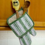 Quilted Decade classic oven mitt and pot holder shown in blue color, hanging with with striped side visible