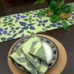 Celebration design Dinner Napkin in green with mint runner LS looking down from hem and tassel