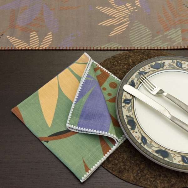 Pollen Up design dinner Napkin in purple with table runner in pollen up design in buff, in background, matt black, black cork placemats, from hem and tassel
