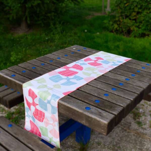 Table runner of flock and flutter design on picnic table in park from Hem And Tassel