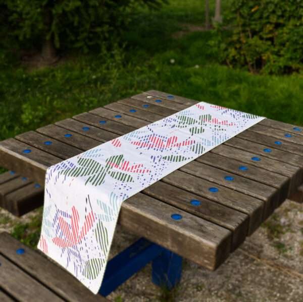 Table runner of pollen and flowers design in pink on picnic table by Hem And Tassel