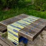 Table runner of yellow piano design on picnic table in park by Hem And Tassel