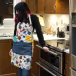 Apron of Flocks & Flutter grey design on woman in kitchen from Hem And Tassel