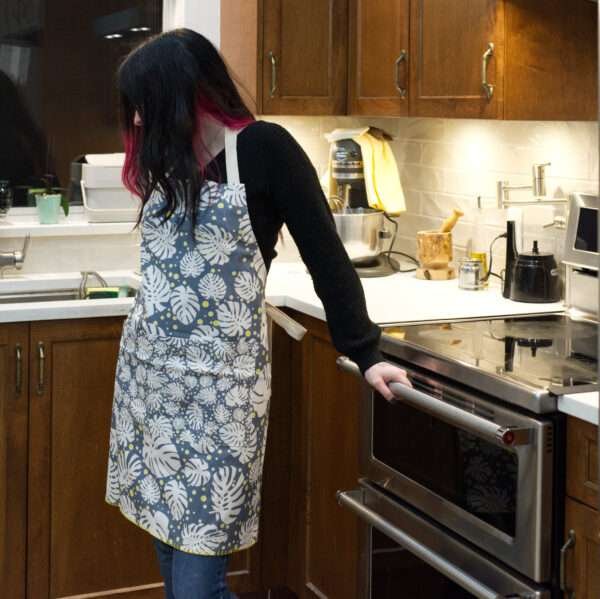 Apron of Monster Ah design on woman in kitchen by Hem and Tassel