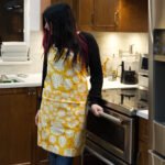Apron of Monster-Ah Orange design on woman in kitchen by Hem and Tassel