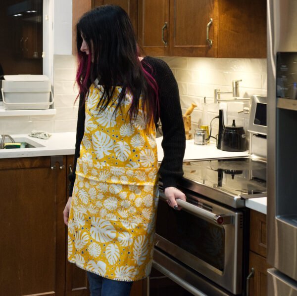 Apron of Monster-Ah Orange design on woman in kitchen by Hem and Tassel