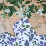 Celebration tea towl in purple on table with leaves and flowers from hem and tassel