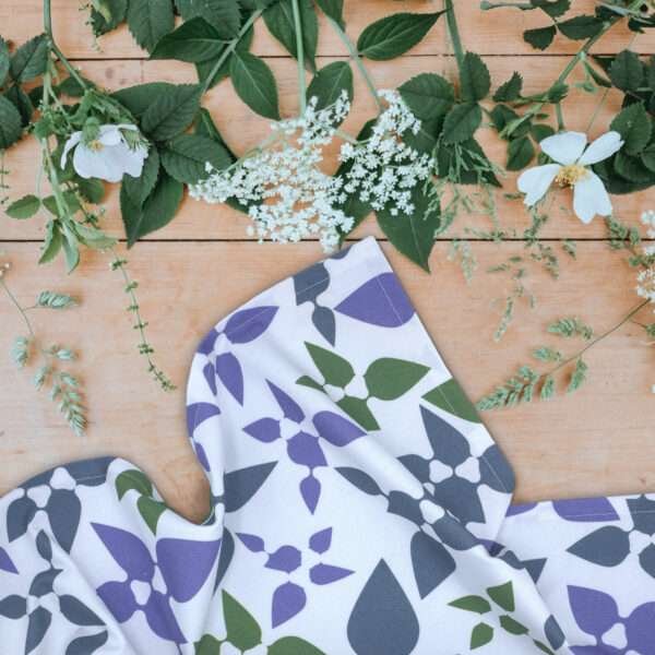 Celebration tea towl in purple on table with leaves and flowers from hem and tassel