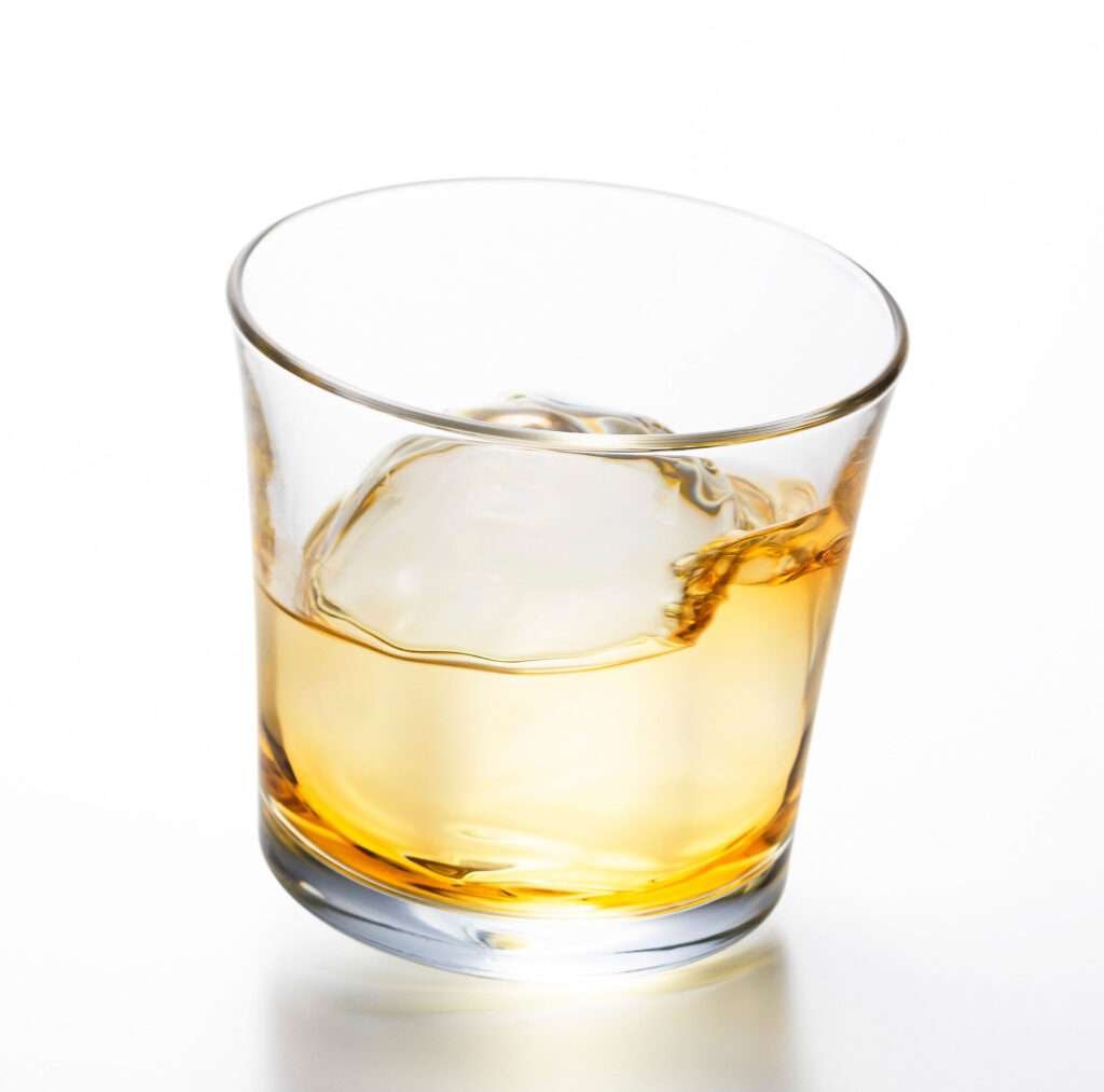 Tottering whiskey glass with drink and ice from hem and tassel